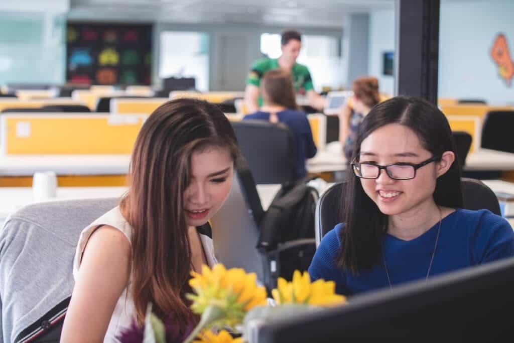Two women sit in front of a computer with flowers how to code for free