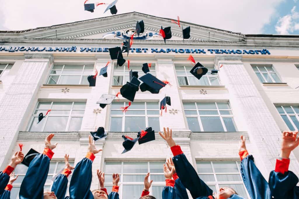  Students tossing their caps during graduation with the university building in the background gis degree programs 