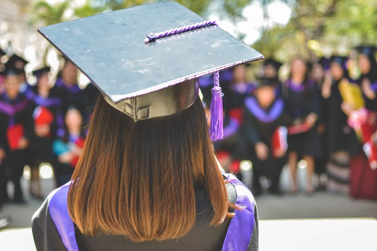 Woman wearing black and purple graduation cap and gown. Coding Bootcamp vs College