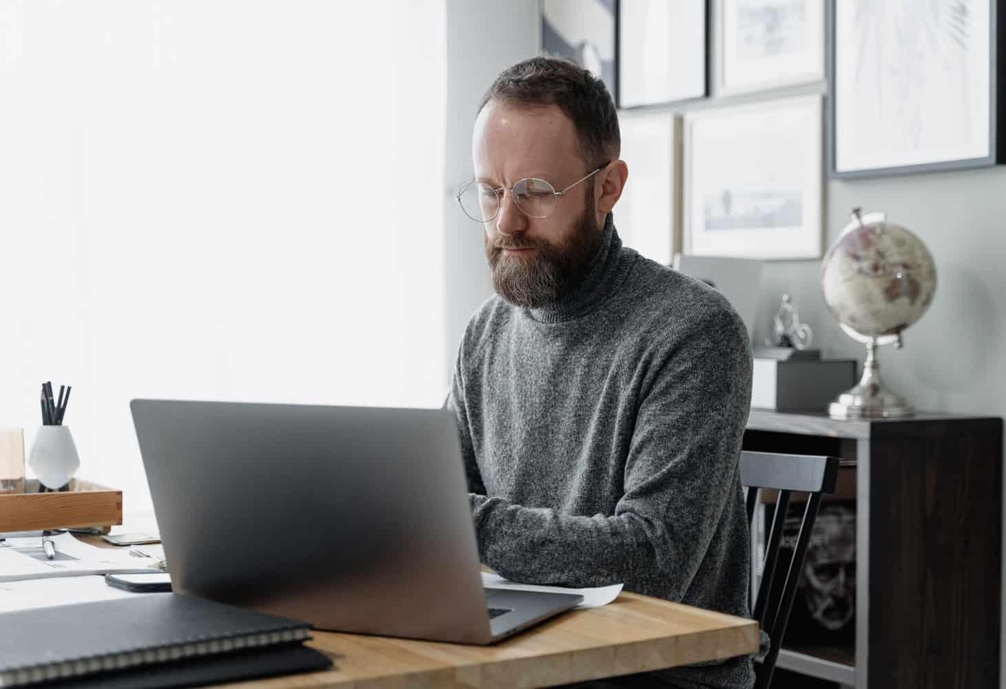 Essential-Network-Administrator-Skills Man in a grey sweater using a laptop. Essential Network Administrator Skills and Certifications