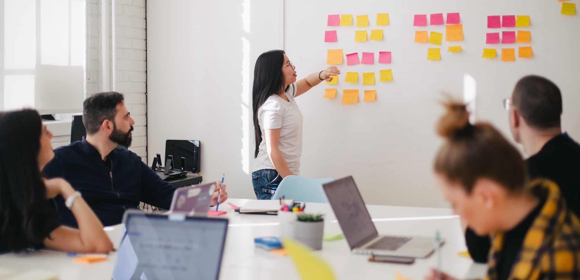Woman placing sticky notes on a whiteboard while facilitating a team meeting. How to Become a Product Manager