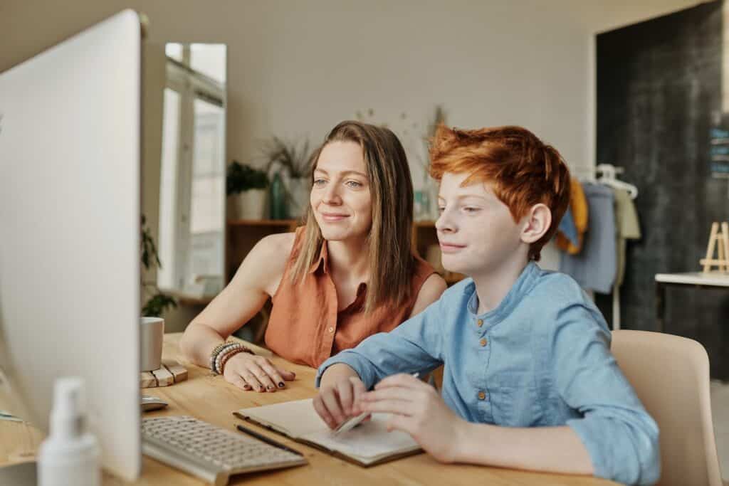 A young boy with his mother in front of a computer monitor.
