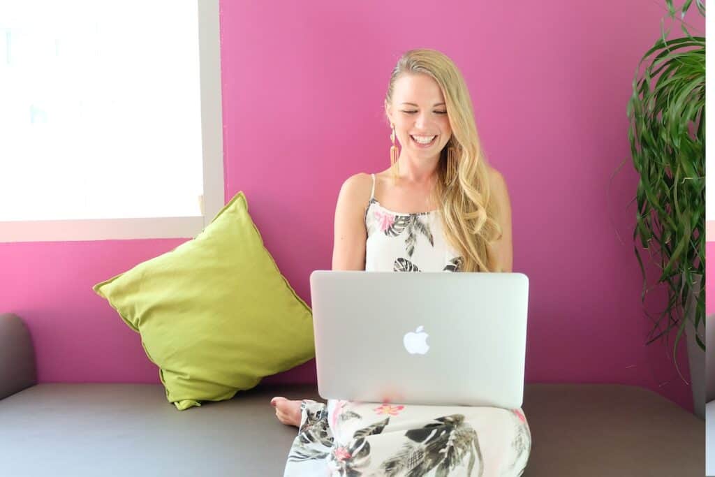 A graphic designer works on laptop    and sitting on sofa against a pink wall
